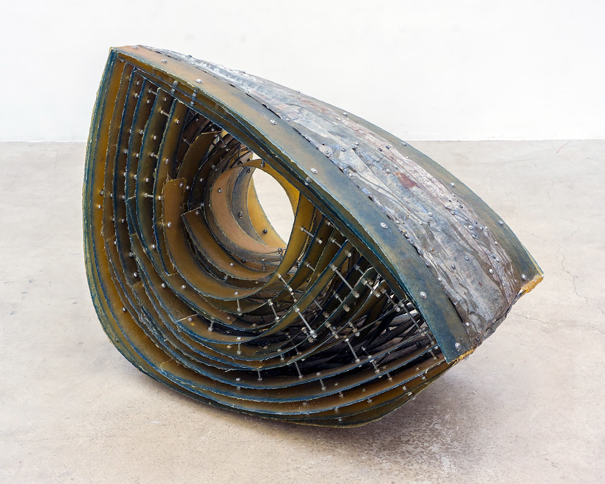Abstract metal sculpture composed of layered, curved steel forms surrounding a circular opening, with rivets and exposed structural elements.