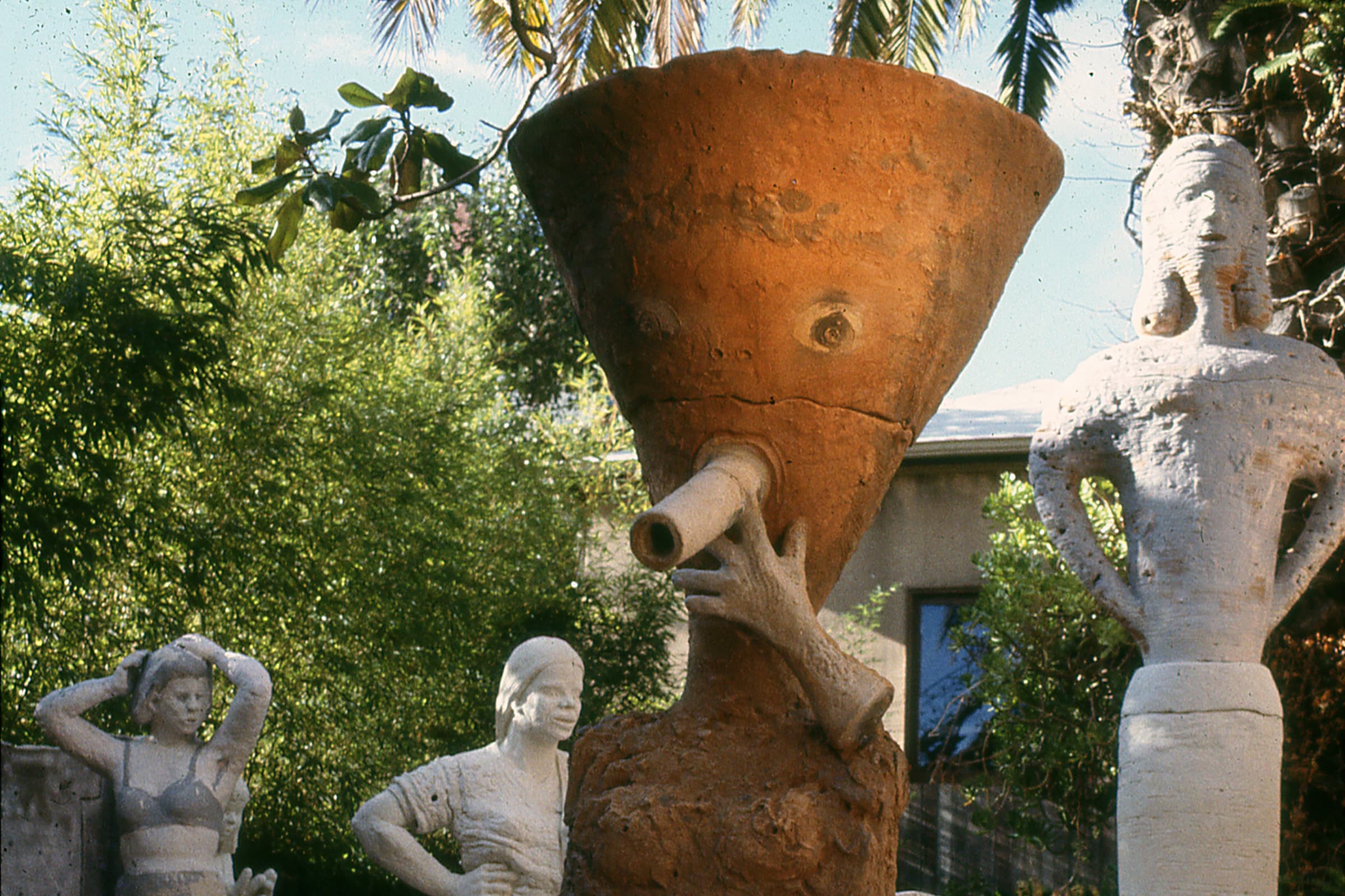 A sculpture featuring a funnel-shaped head with painted eyes and a pale pipe-like object extending from its mouth.