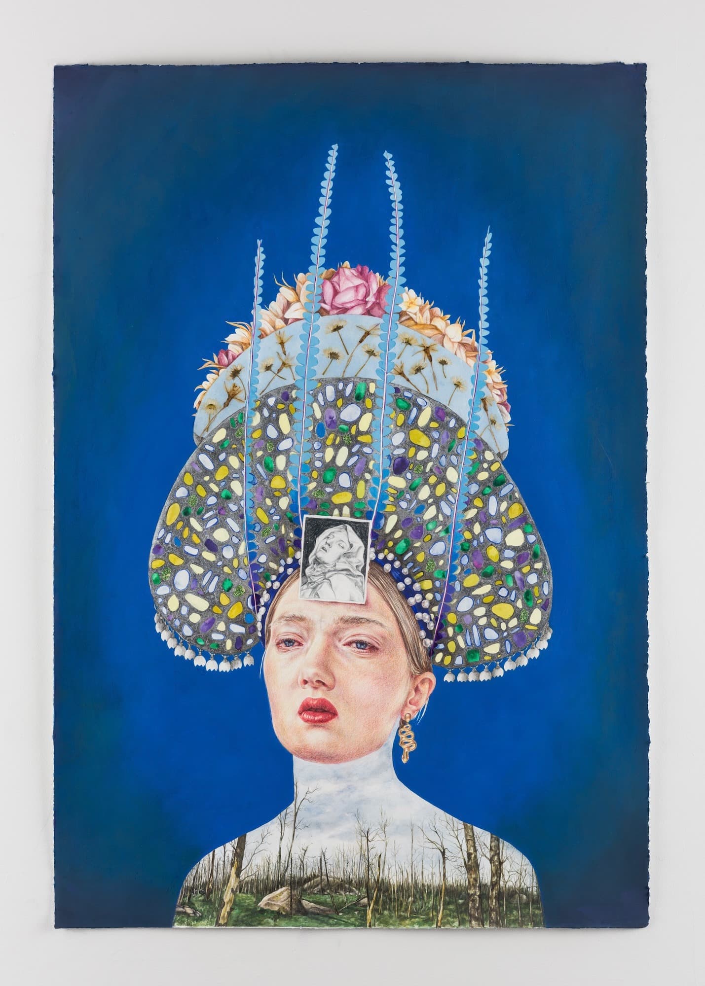 A mixed-media portrait of a woman against a solid deep blue background. She wears an immense, elaborate headdress decorated with colorful mosaic tiles, pink roses, and tall feathers. Her neck and shoulders transition into an illustration of a dense, bare winter forest. A small, black-and-white sketch of a classical face is pasted onto her forehead.