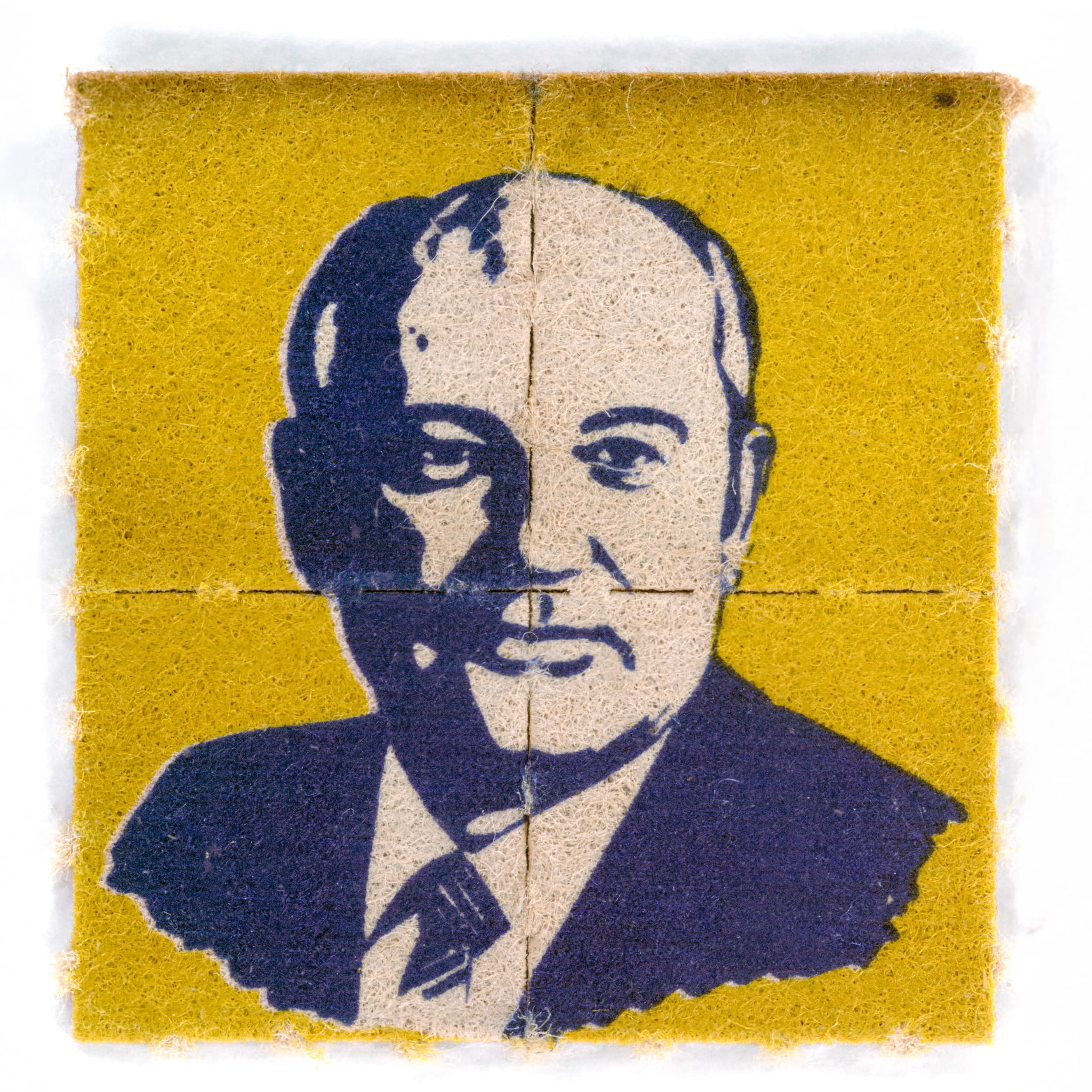 A square piece of yellow blotter paper divided by faint cross-perforations into four smaller squares. A stylized, high-contrast portrait of Mikhail Gorbachev is printed across the sheet in dark blue ink.