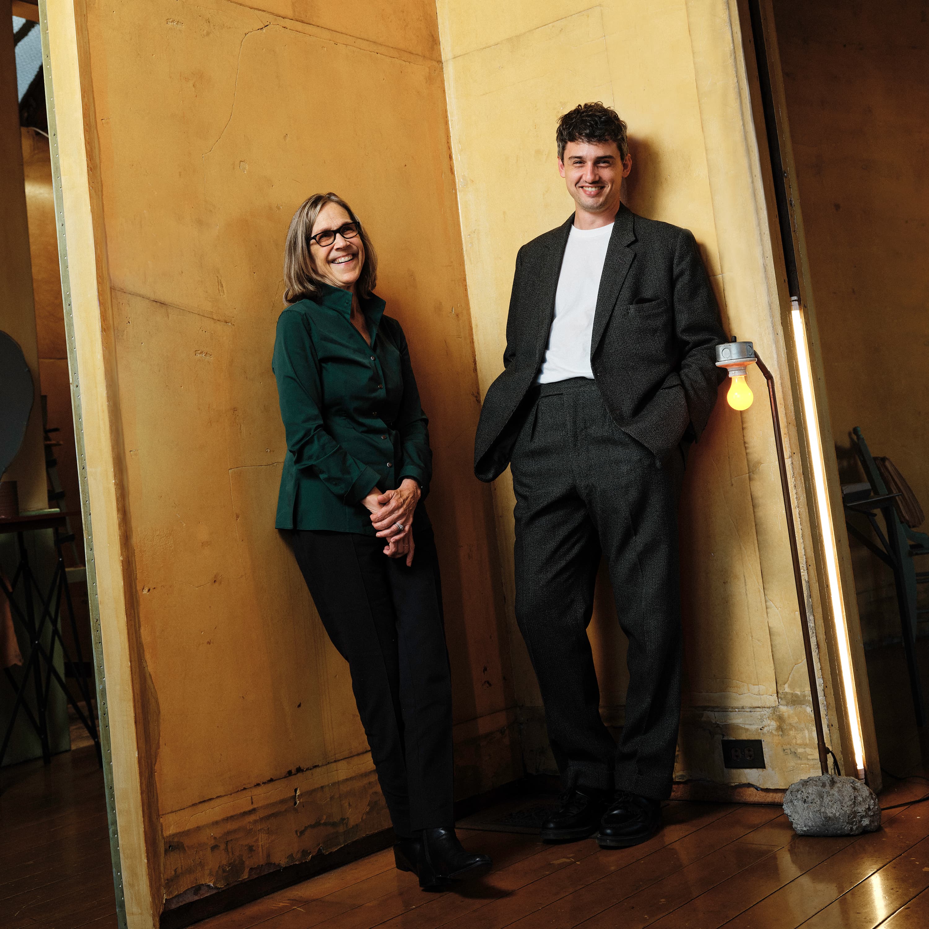 Photo featuring Robin Wright and Zully Adler, the Founder and Executive Director of Further Triennial respectively. They stand side by side looking at the camera, leaning against a yellow corner at 500 Capp St.