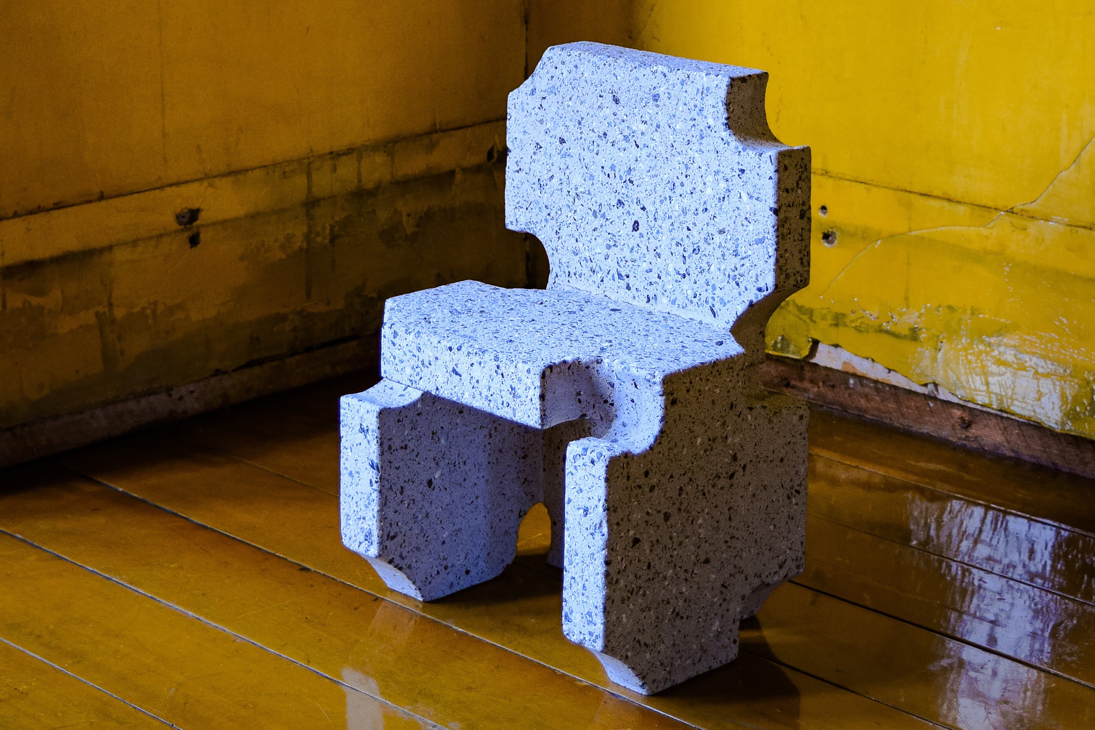 A small cement chair sits on the corner of yellow-varnished room.