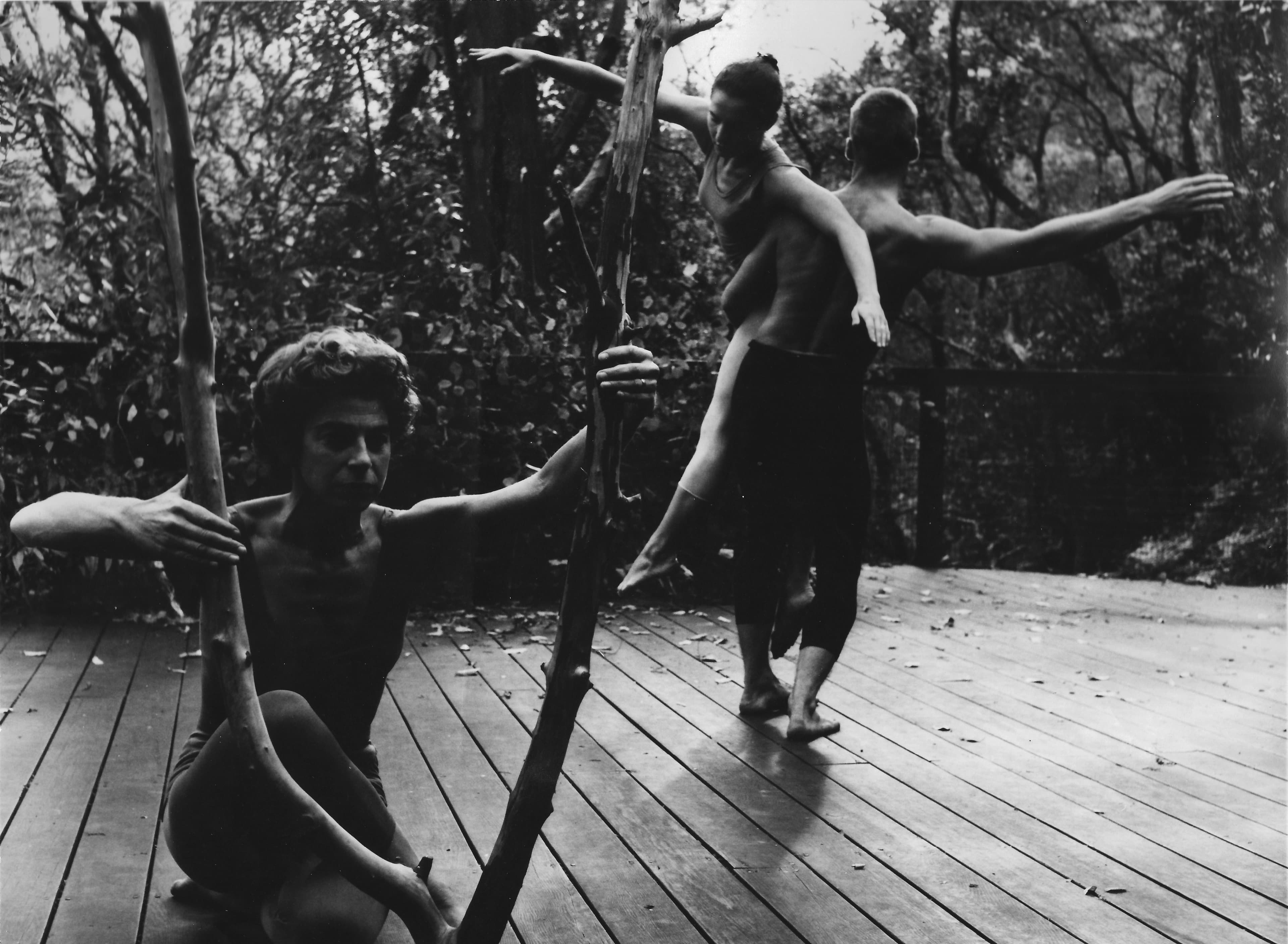 A black-and-white photograph of Anna Halprin with dancers Simone Forti and A.A. Leath performing The Branch on the Halprin Dance Deck in Marin County in 1957. The three figures are shown moving together on the outdoor wooden dance deck, surrounded by the natural landscape. The photograph captures the early experimental, site-responsive approach to movement that characterized Halprin’s work. The photograph is 8 × 12 inches. Courtesy of Warner Jepson, the Museum of Performance + Design, and Halprin Legacy Lab photo by Warner Jepson.