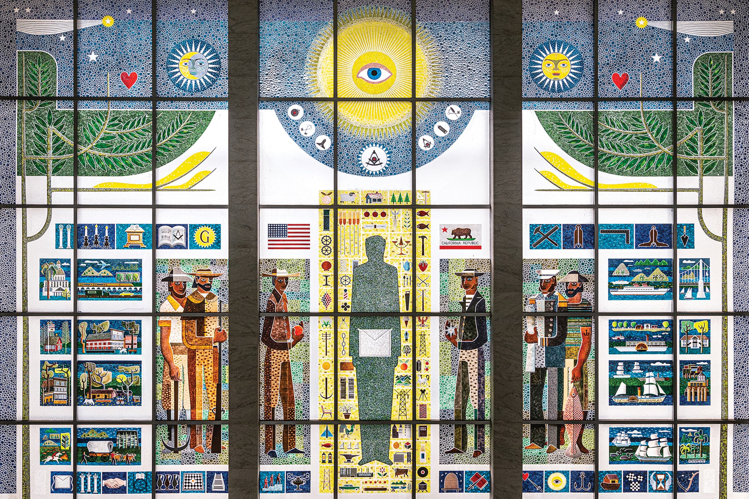 A detailed three-panel window endomosaic captures the history, culture, and industry of California. The left and right panels feature matching stylized green trees under celestial skies with smiling suns, crescent moons, and shooting stars, framing vignettes of historic buildings, agriculture, modern shipping, and engineering like a suspension bridge. Figures of historical men, a naval officer, and a fisherman flank these outer panels. The central panel is dominated by a large yellow sun containing a prominent eye above a masonic square and compass, with a tall green silhouette of a man holding an envelope standing between a farmer with an American flag and a sailor with the flag of the State of California.