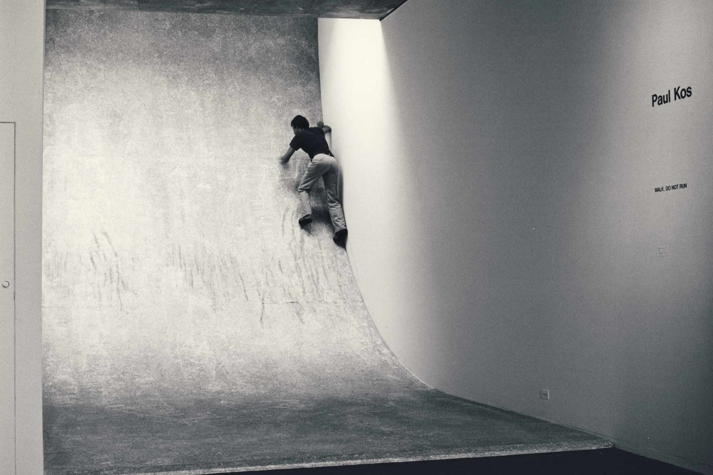 A man climbing a wooden ramp in an enclosed room of the same width as the ramp itself.