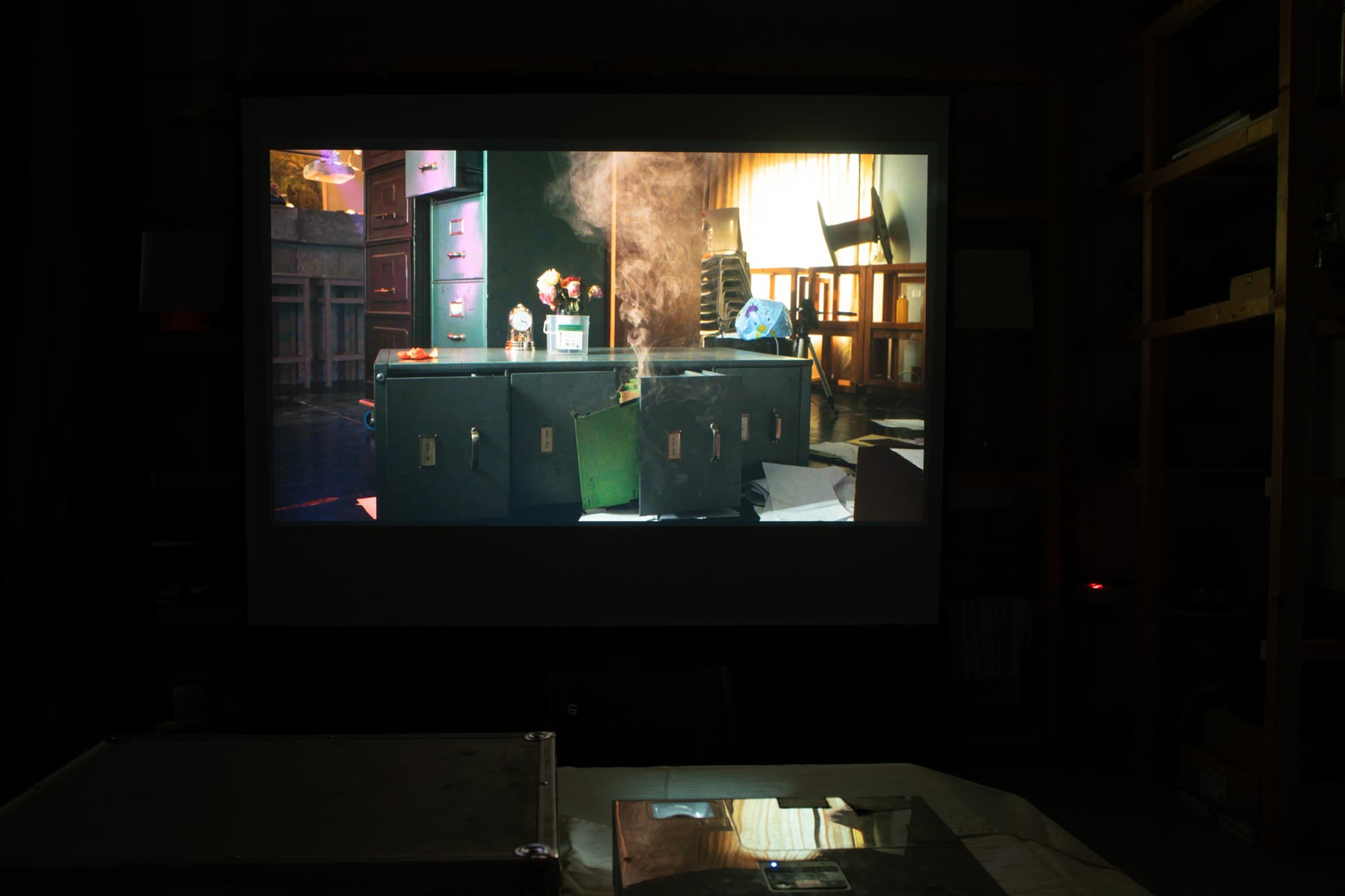 Image of a video installation showing a still in which smoke is emerging from a green file cabinet.