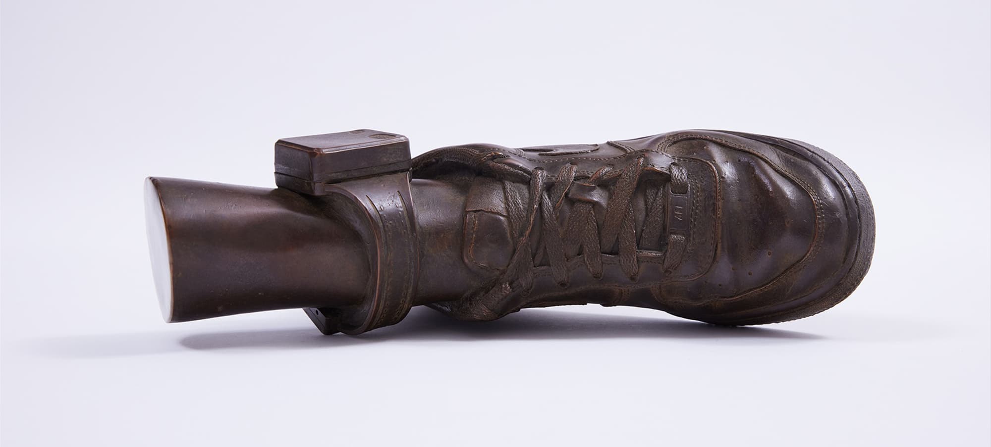 A bronze life size sculpture of a sneaker-clad foot wearing an ankle monitor.