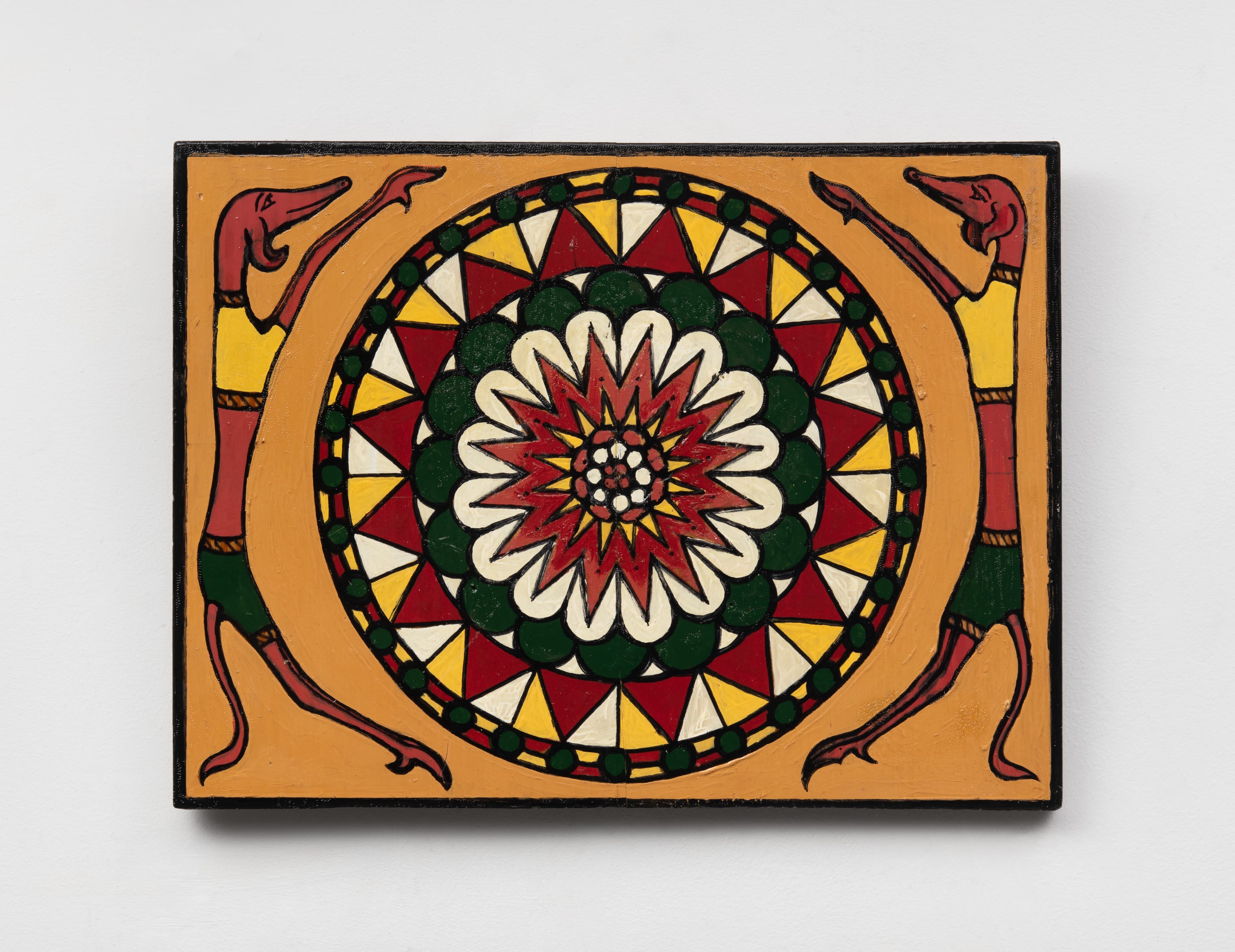 A vibrant, geometric painting featuring an intricate mandala framed by two stylized creature-like dogs. The mandala consists of concentric rings of red, green, yellow, and white triangular and petal-like patterns radiating outward from a flower-like core. Flanking this circular design on a warm ochre background are two thin, elongated, reddish-brown figures resembling greyhounds or jackals standing on their hind legs. The creatures face inward toward the mandala with their front paws raised, wearing yellow shirts and green shorts with dark patterned waistbands.