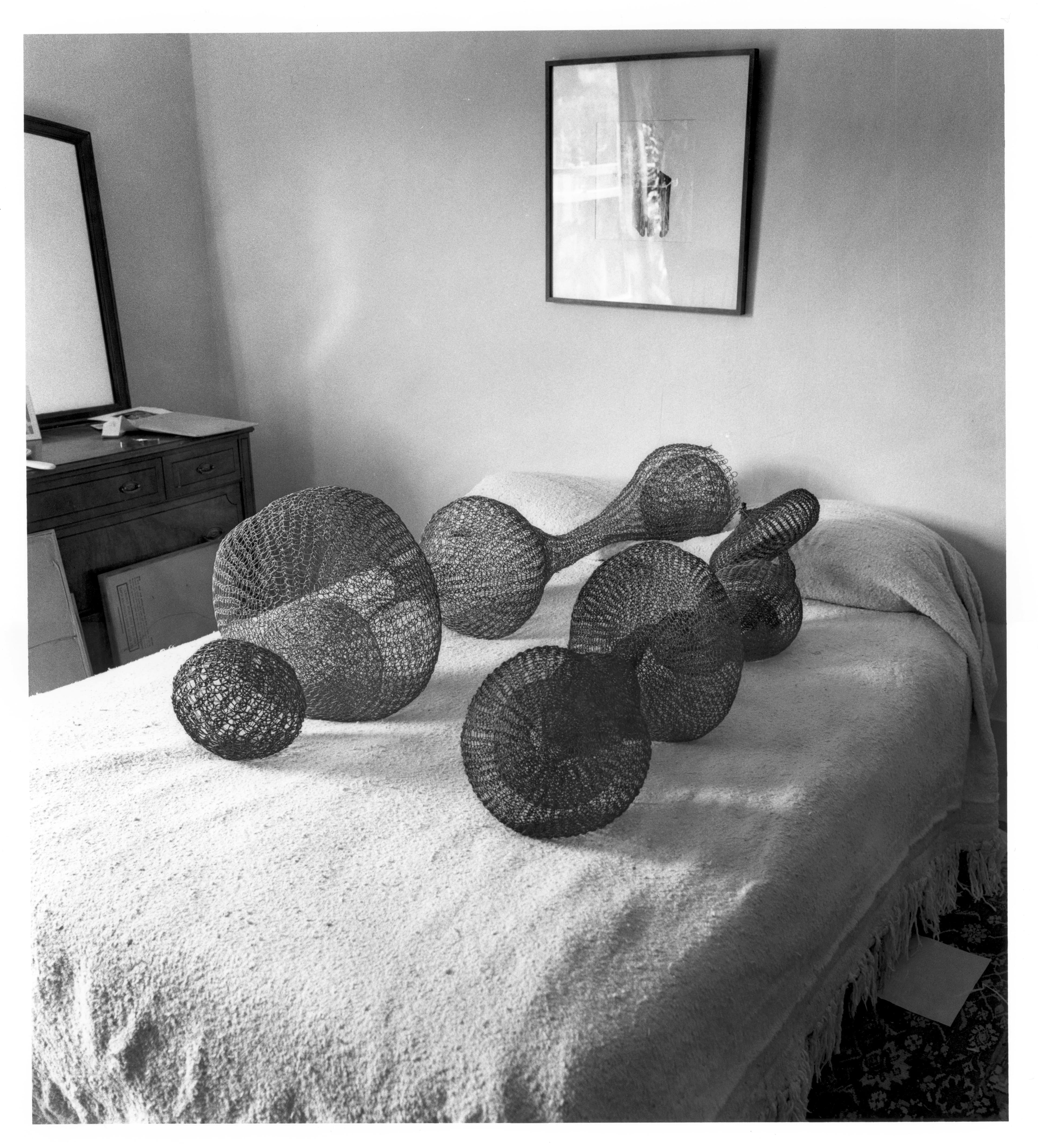 Black and white photo of two of Ruth Asawa's looped-wire sculptures laid on the bed of Ruth Asawa and Albert Lanier to evoke reclining figures.