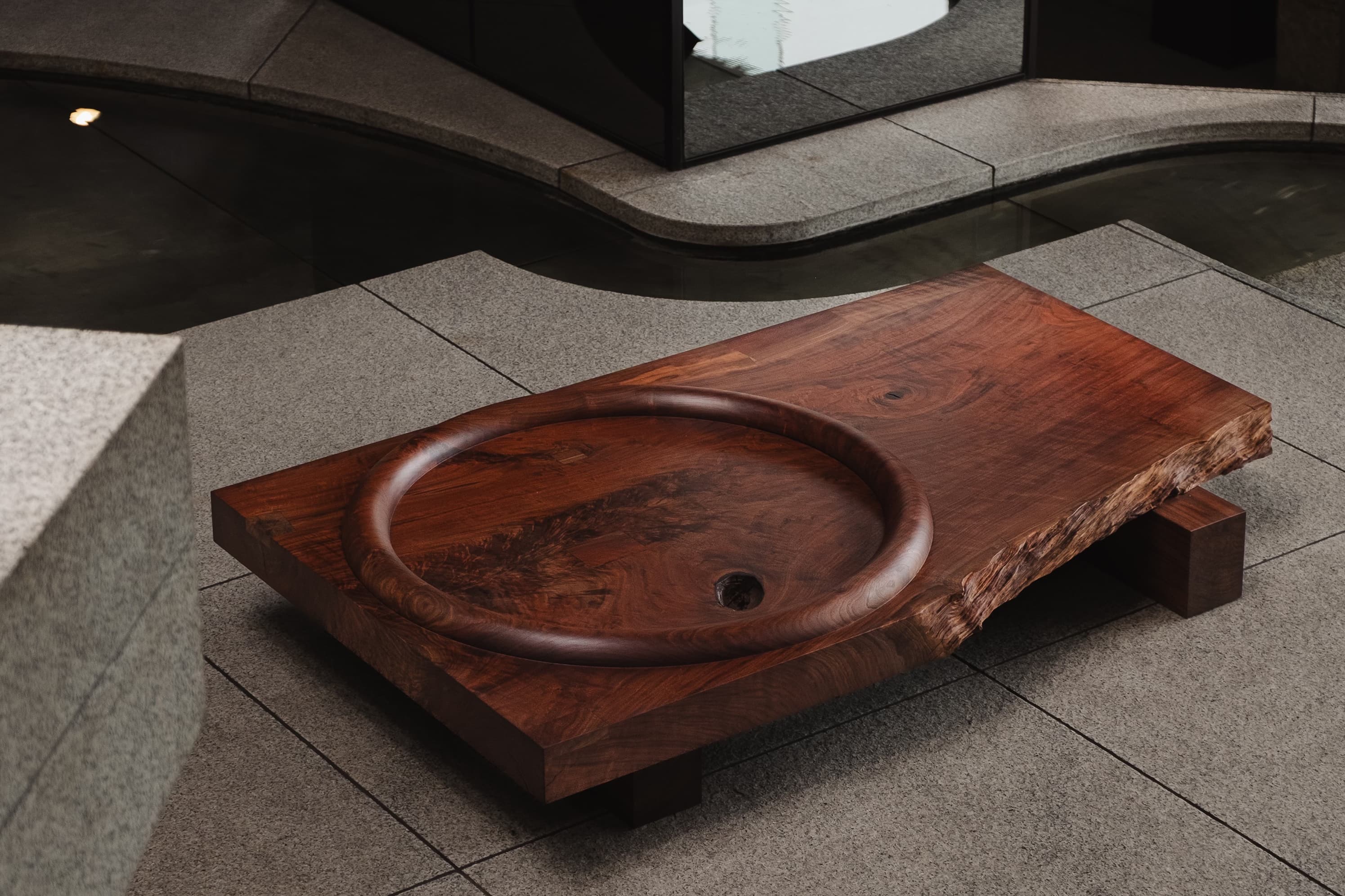 A slab of walnut wood sits on another board of wood and has a circular imprint on the top face.