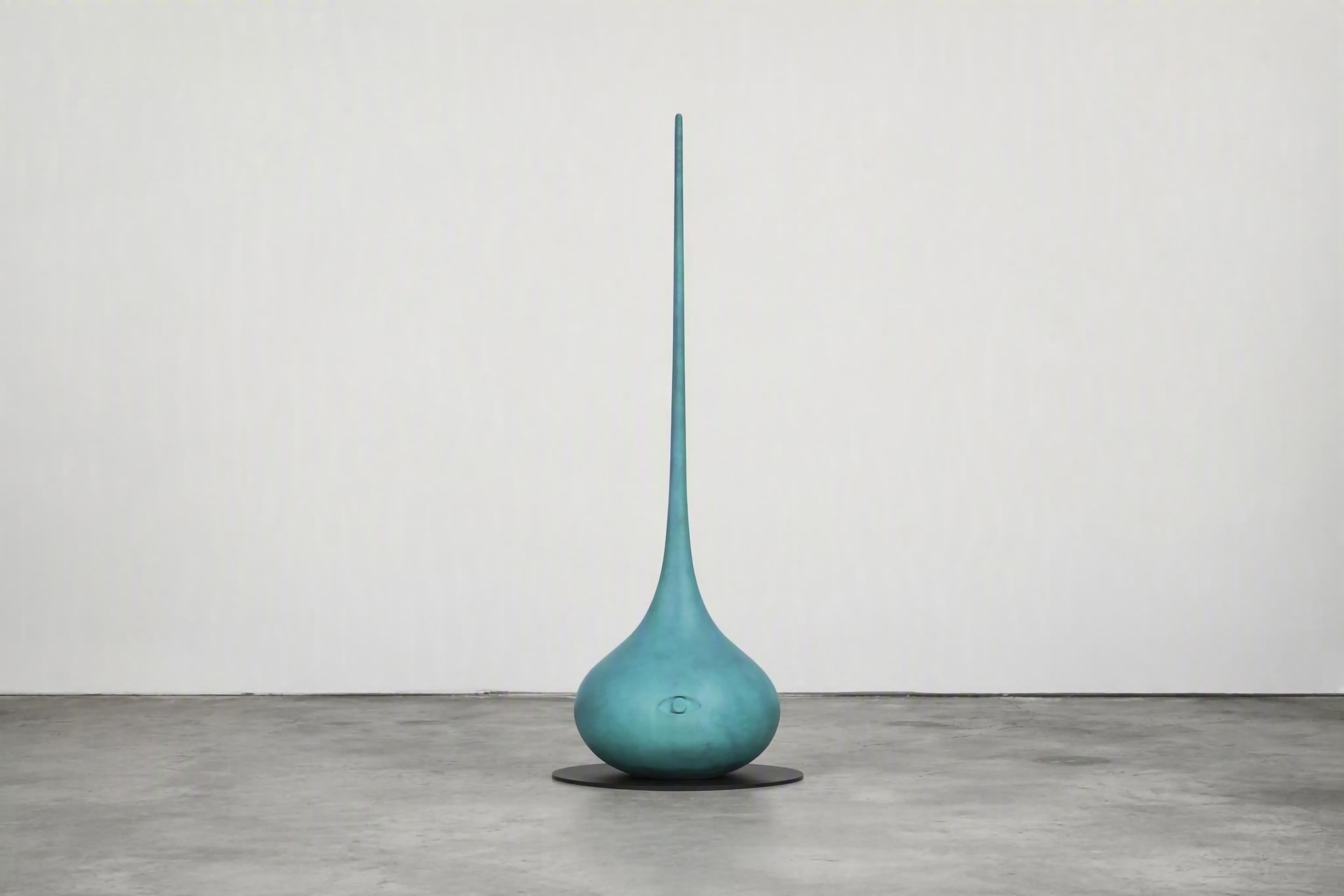 Tall turquoise sculptural vessel with a rounded base, long tapered neck, and an eye motif near the bottom.