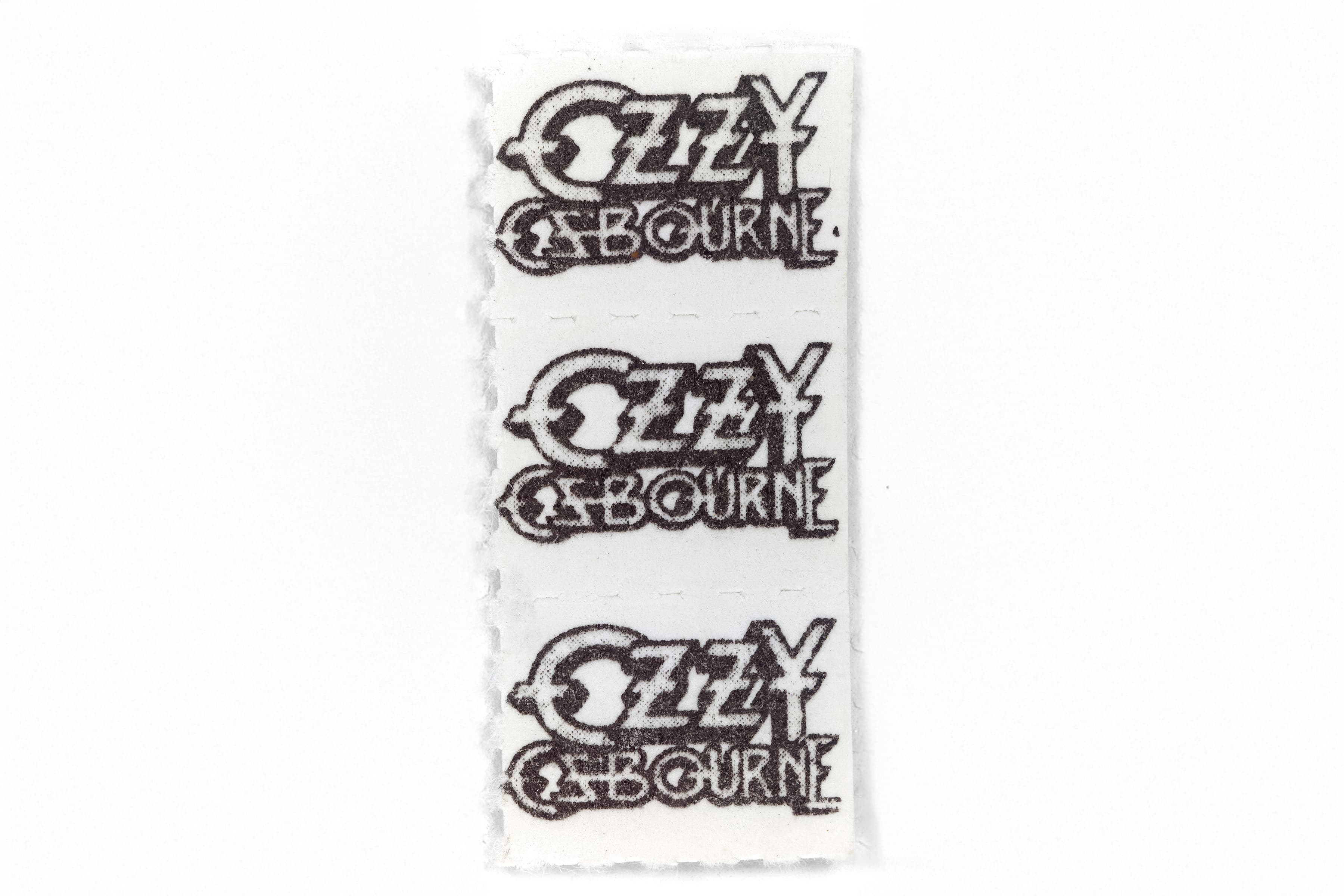 A vertical strip of white blotter paper containing three perforated segments. Each segment features a black-and-white stamp of the stylized "Ozzy Osbourne" band logo.