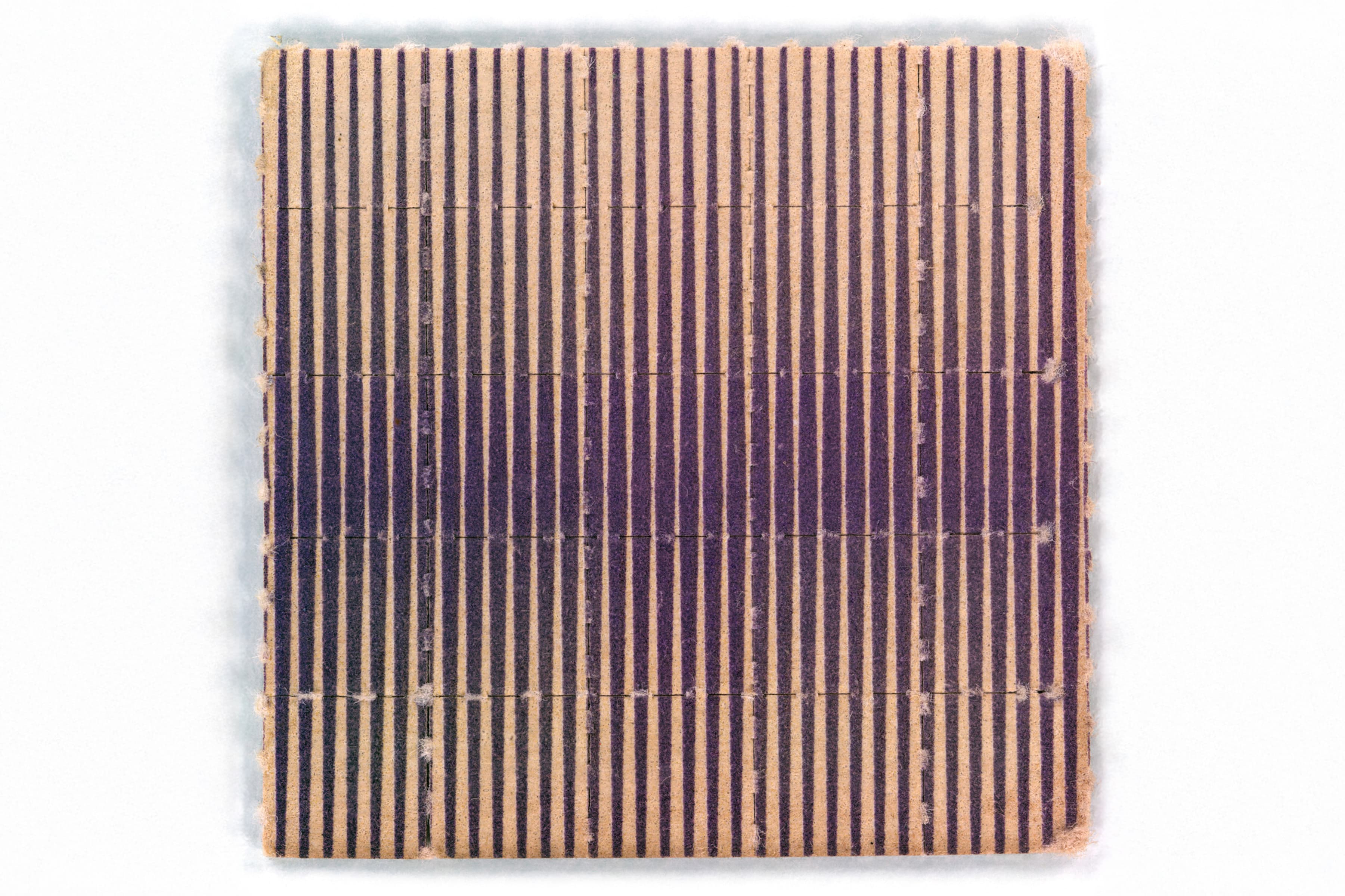 A square piece of blotter paper with a dense pattern of vertical purple lines on a tan background. Faint grid-like perforations are visible across the surface, and the purple coloration darkens toward the horizontal center of the sheet.
