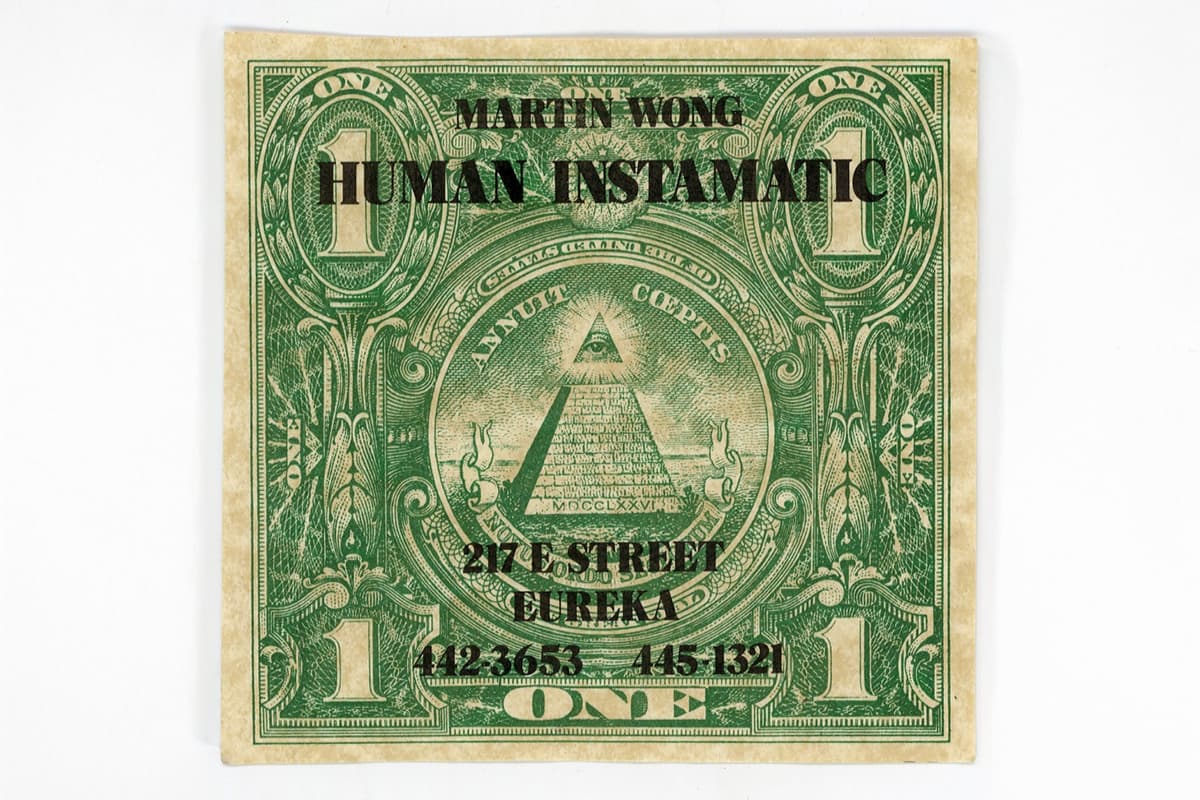 A graphic art print resembling a modified green United States one-dollar bill. The center features the iconic Eye of Providence pyramid from the Great Seal. Stamped over the top and bottom in bold, black block lettering is the text: "MARTIN WONG HUMAN INSTAMATIC" at the top, and "217 E STREET EUREKA 442-3653 445-1321" at the bottom, mimicking a vintage business card or promotional stamp.