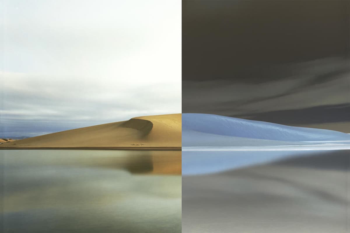 A split-screen artwork showing the same sand dune beside a still body of water rendered twice: on the left in natural color with a golden dune, pale hazy sky, and calm reflective water, and on the right as a color-inverted negative, turning the dune blue-white and the sky dark brown-gray.