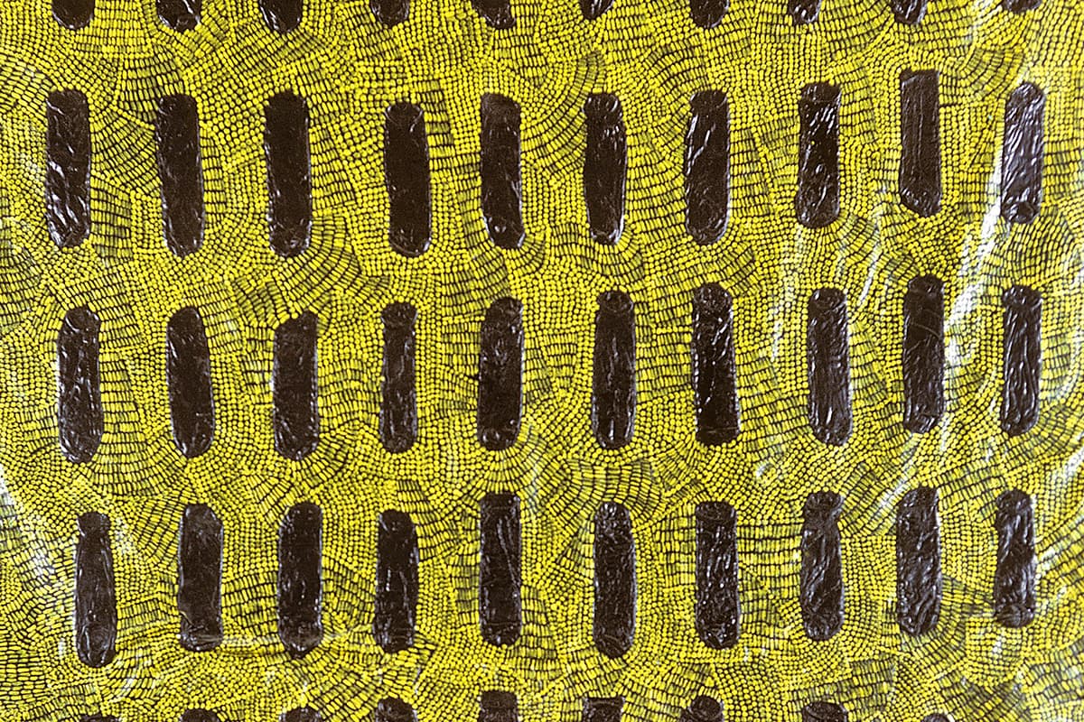 A large, translucent yellow-gold latex sheet on cheesecloth, covered with rows of vertically arranged condoms embedded in its textured surface.