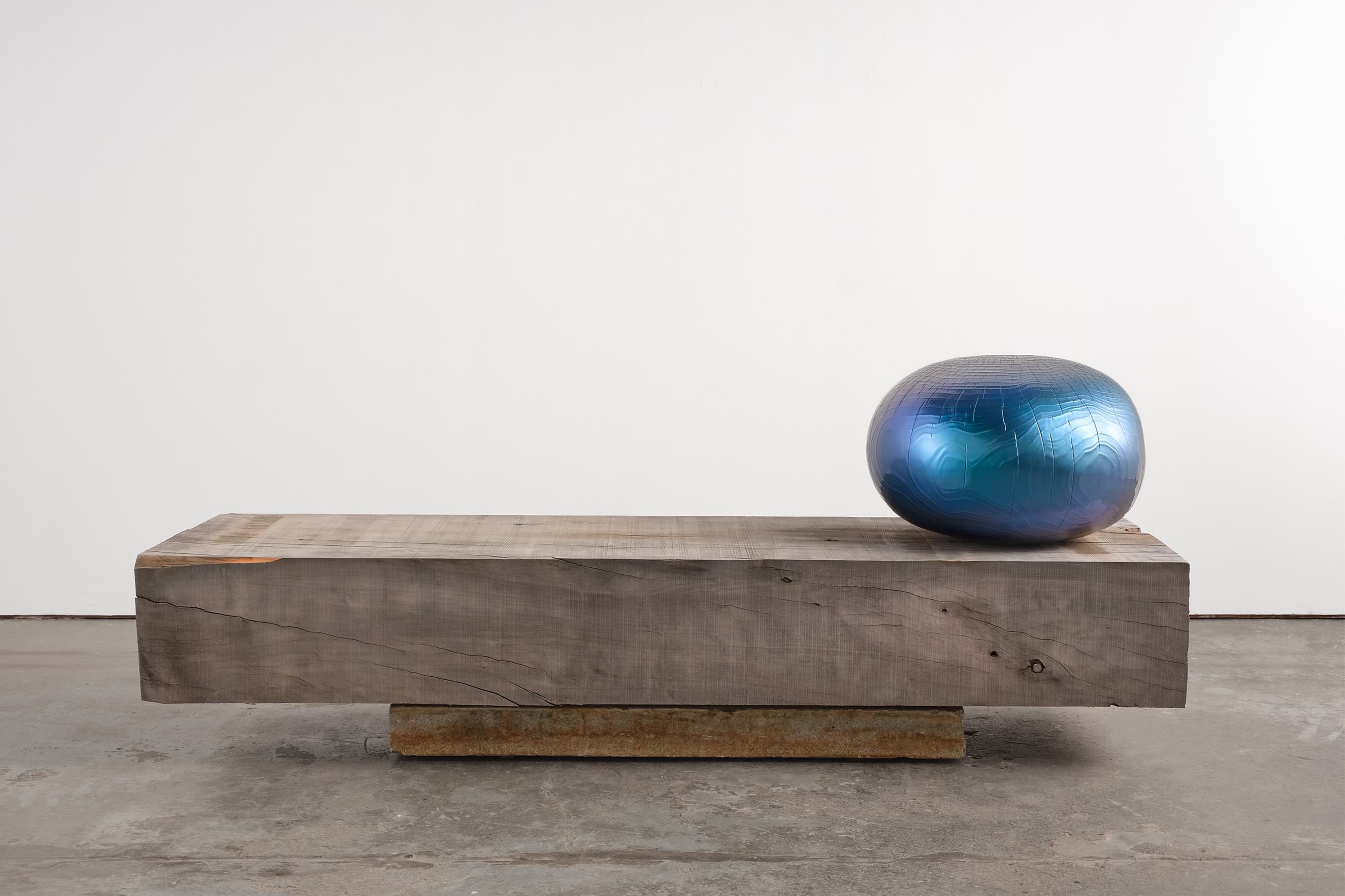 A shiny blue-painted wood sphere sits on the right side of a rough wood bench.