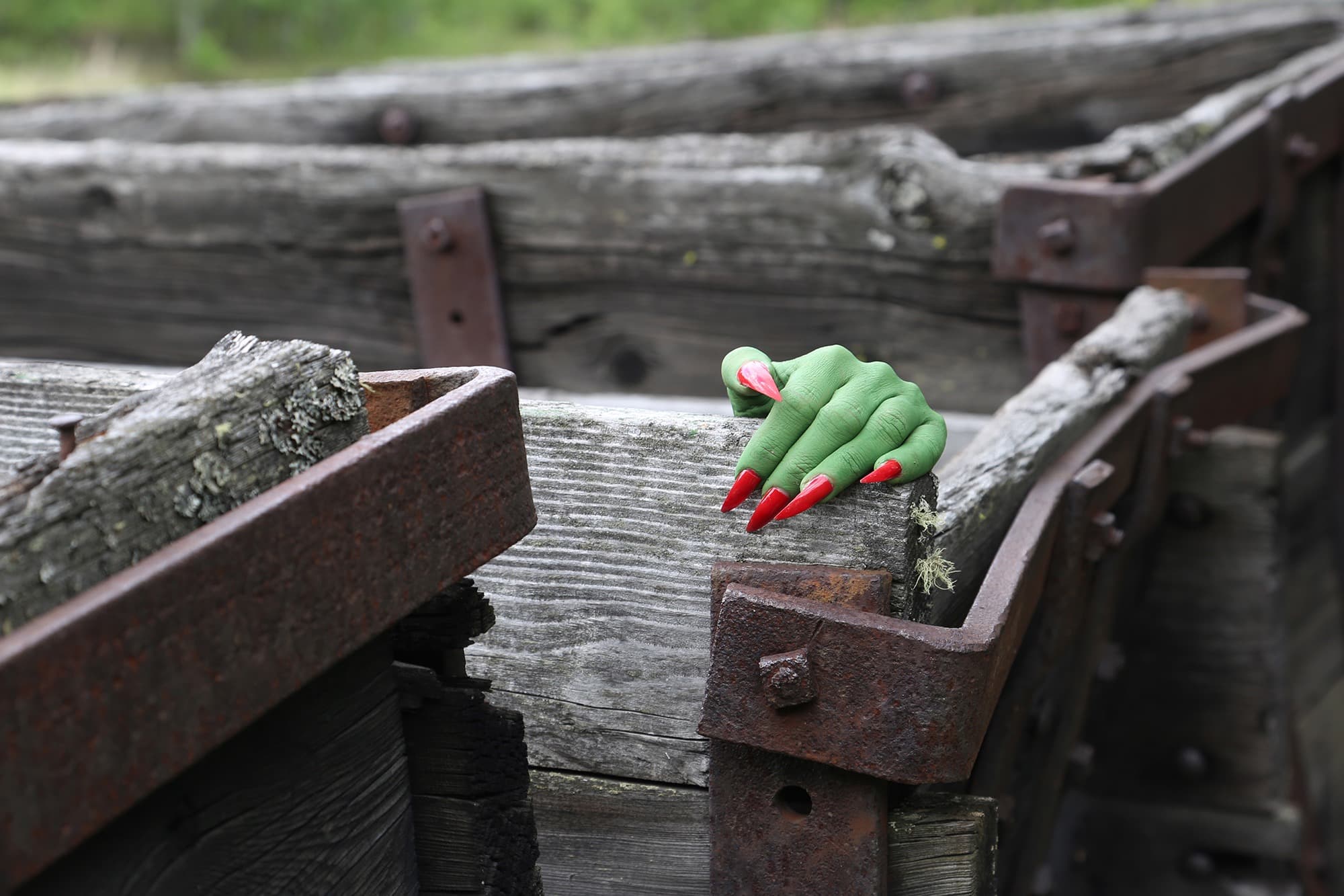 A green hand with long red nails grabbing a grey, wooden box with metal.