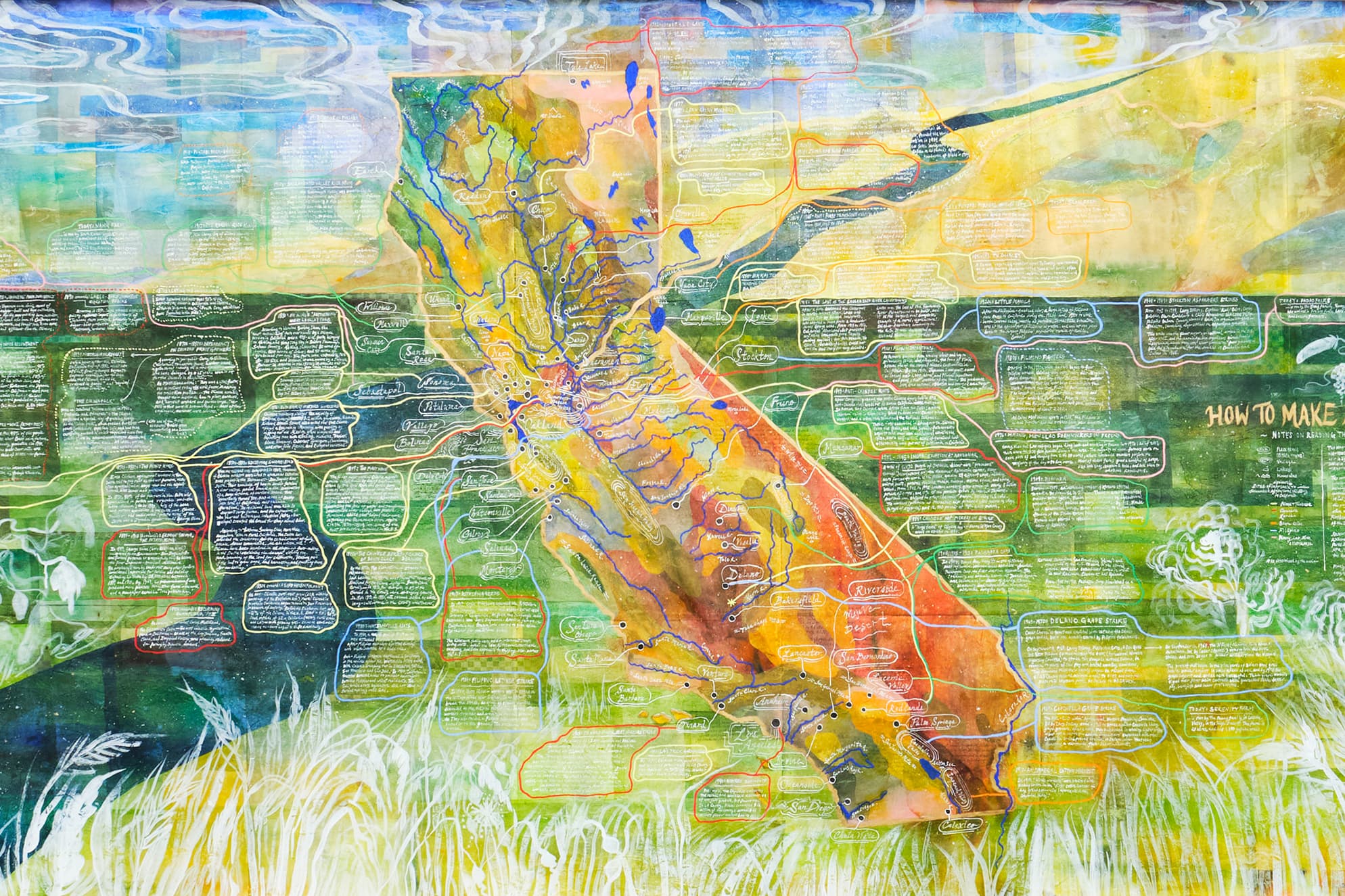 A panoramic mixed-media map collage on paper, displayed on a clean white museum wall. The artwork features an expansive, multi-layered cartographic landscape filled with abstract earth-toned washes, detailed ink drawings, translucent paper overlays, and legible text blocks documenting history.